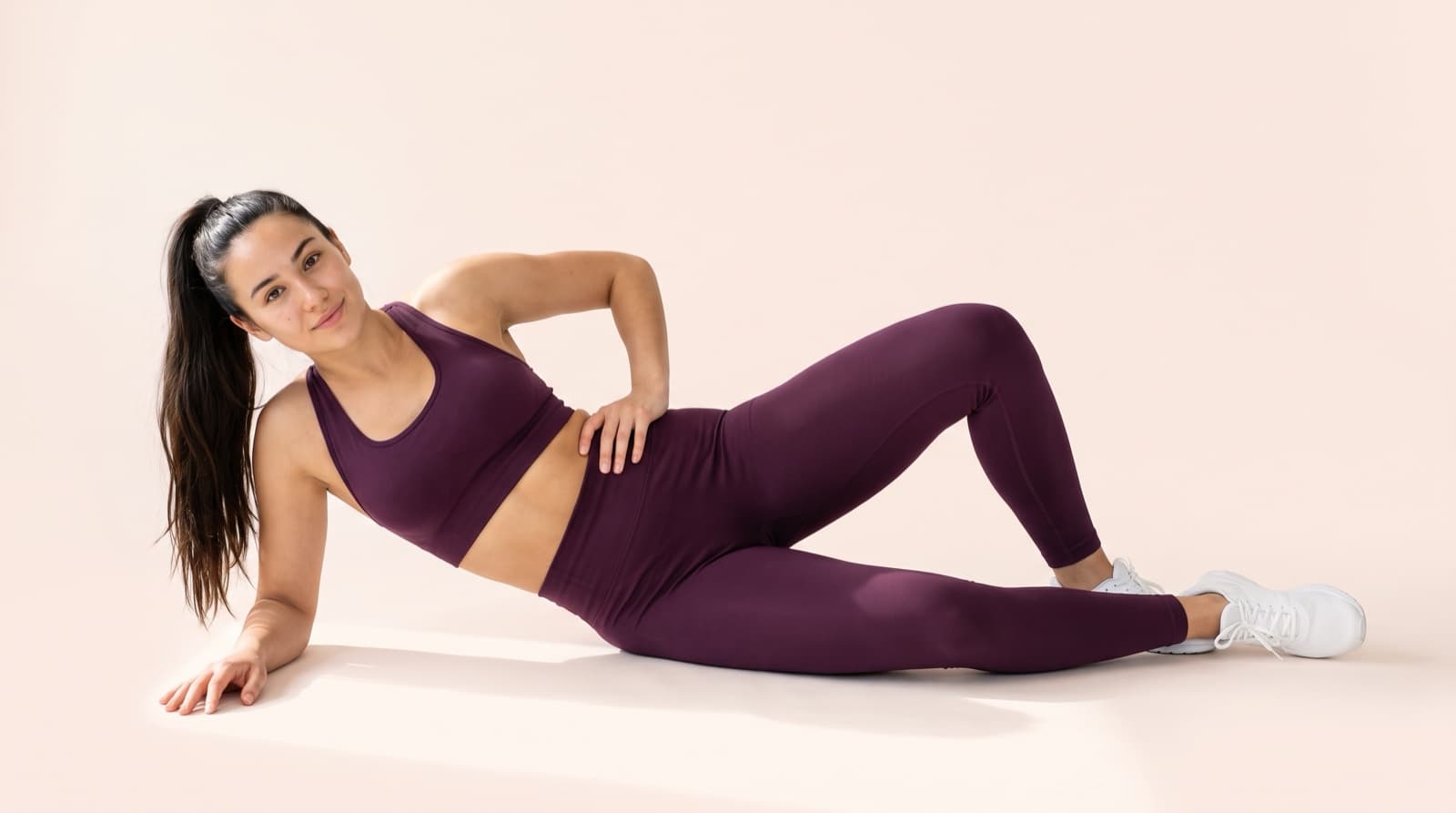 A woman in a plum training set resting on one elbow in a bright studio